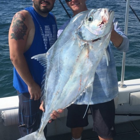 Anglers holding a large African pompano aboard a fishing charter boat in open waters