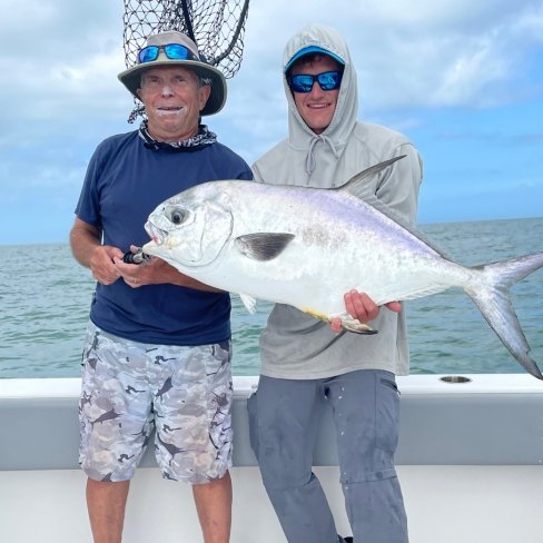 Two anglers holding a large permit fish aboard a fishing charter boat on calm waters.