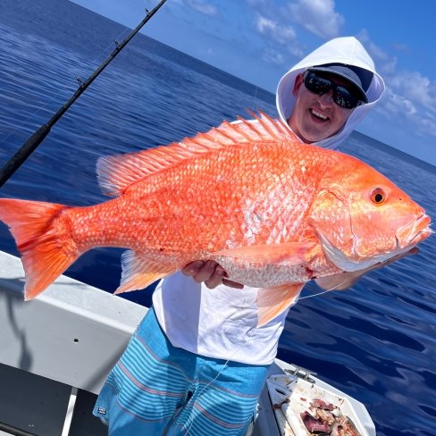 Angler holding a vibrant red snapper aboard a fishing charter boat on calm blue waters.